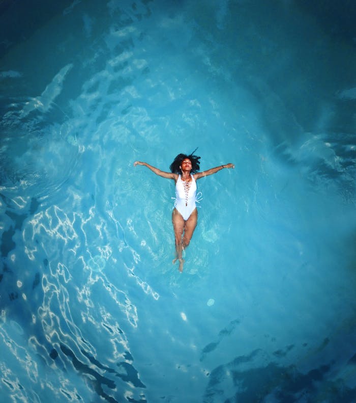gallery-6 An African American woman in a swimsuit floats peacefully in a clear blue swimming pool.