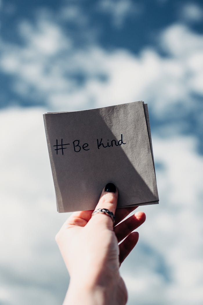 gallery-5 A hand holding a note with '#Be kind' inscribed, set against a bright sky.